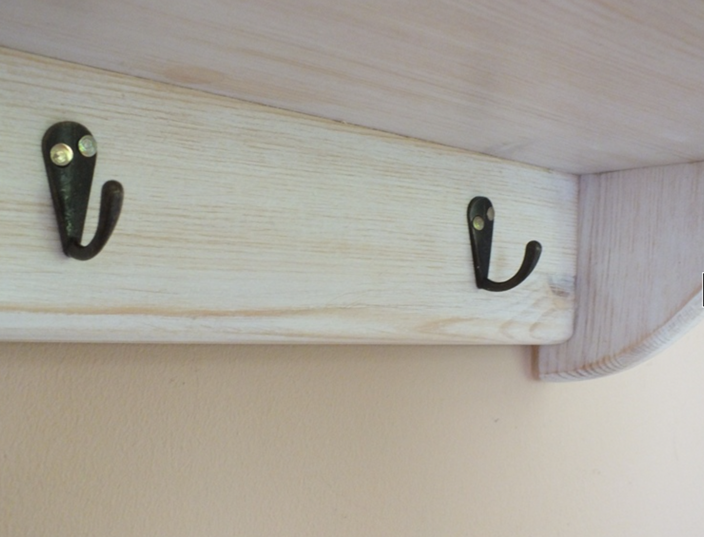 Two black hooks on a wooden shelf against a beige wall.