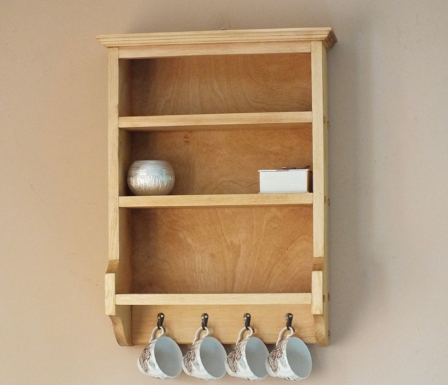 Wooden wall shelf with hooks holding cups against a beige wall.