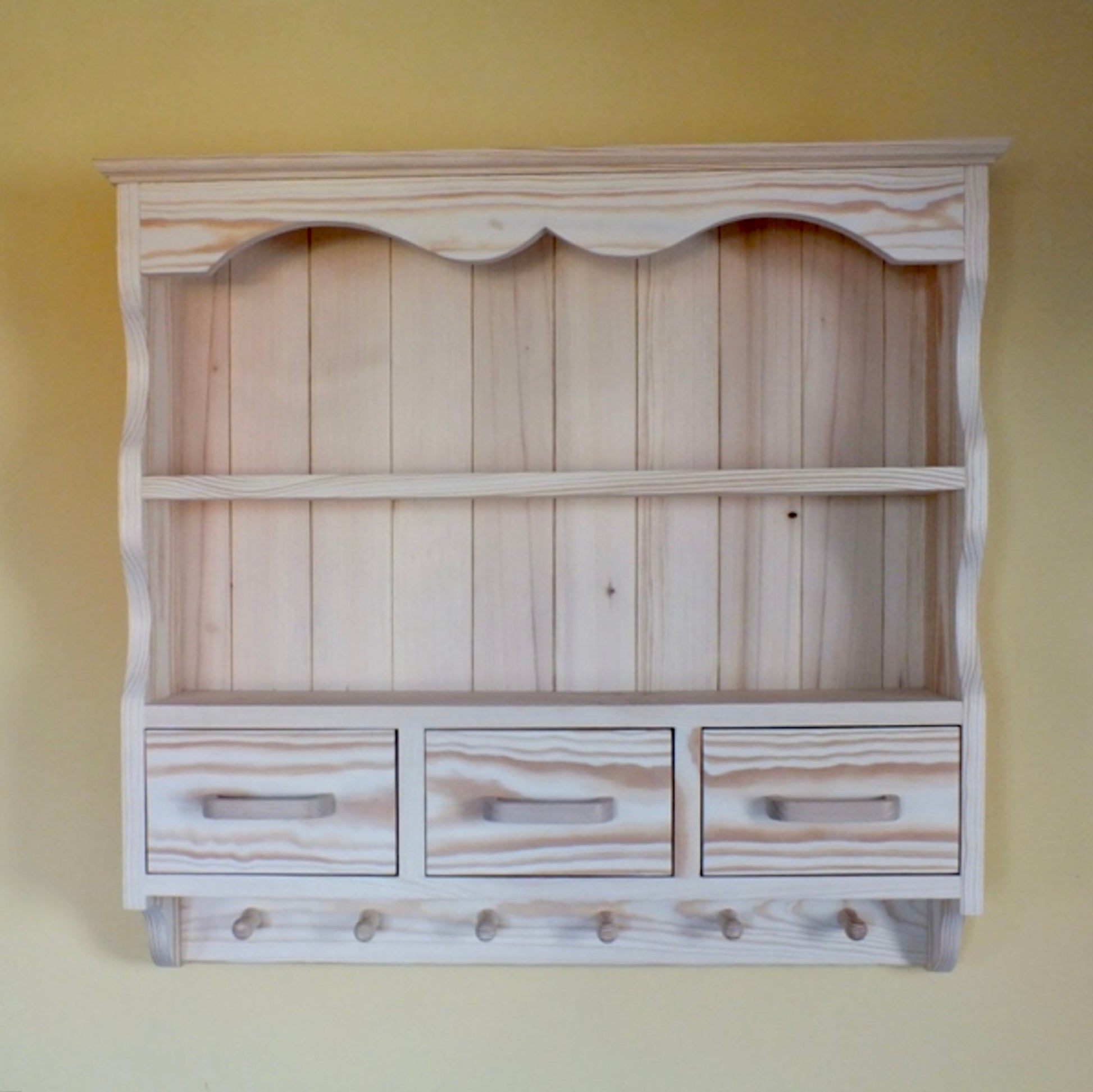 Wooden wall shelf with drawers and hooks on a yellow wall