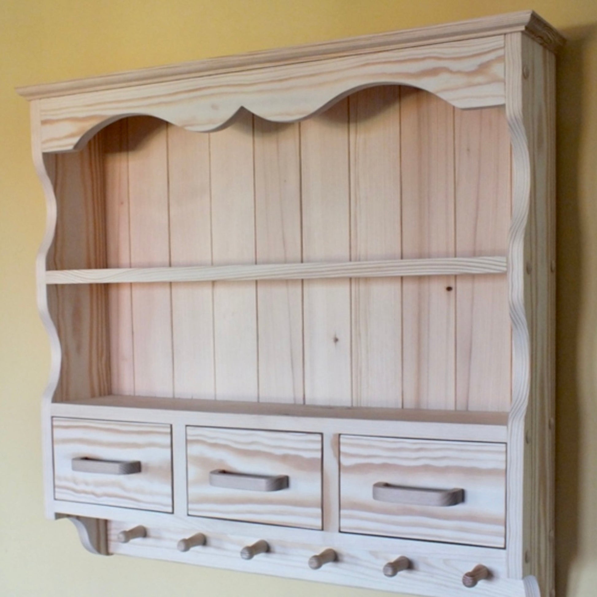 Wooden wall-mounted cabinet with shelves and drawers against a yellow wall.