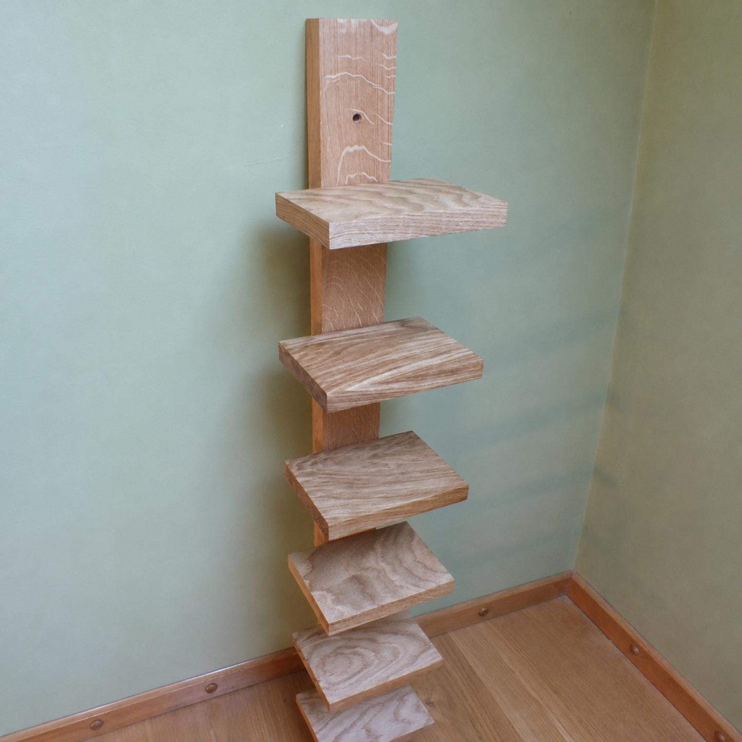 A rustic five-tier wooden shelf unit made from natural oak wood, mounted against a sage green wall in a room corner.