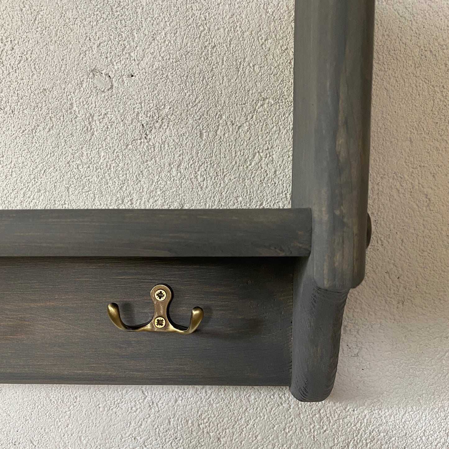 Dark wooden shelf with a gold hook on a light gray wall.