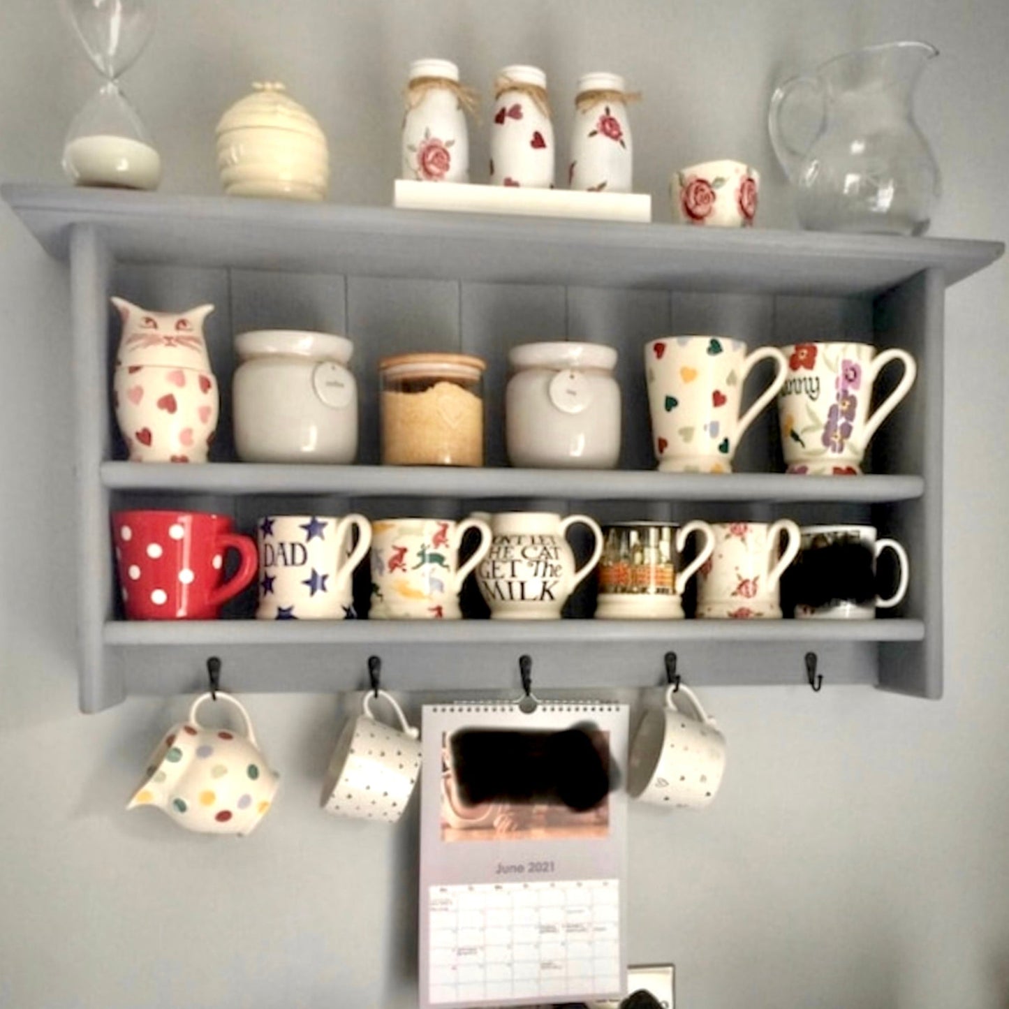 Gray shelf with various decorative items including mugs and jars on a gray wall.