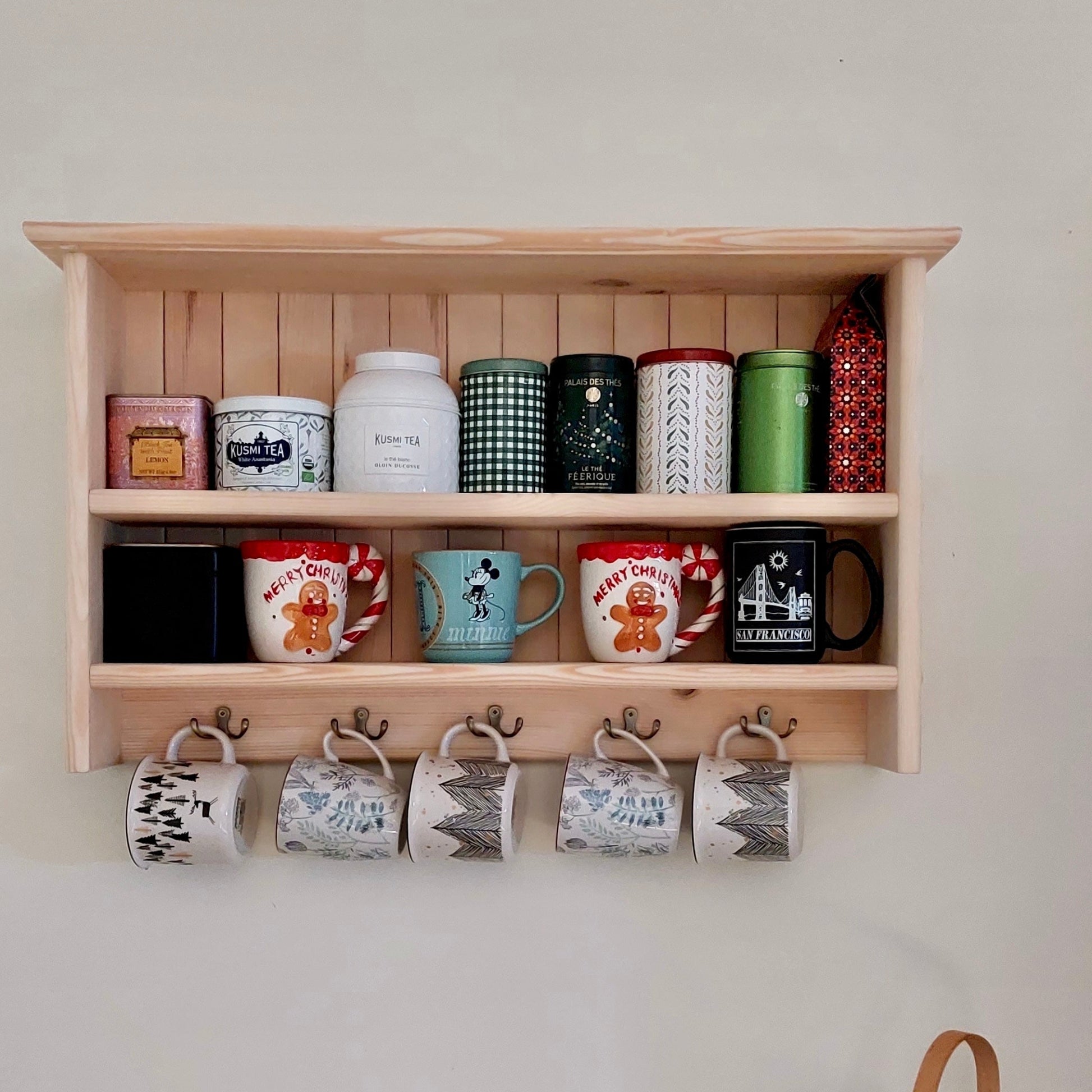 Wooden shelf with various mugs and a woven basket on a light-colored wall.