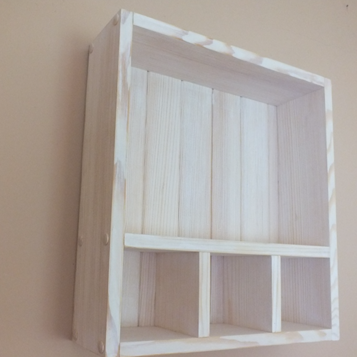 A small white-painted wooden wall shelf with a single horizontal隔板 dividing the space into two sections, mounted on a beige wall.