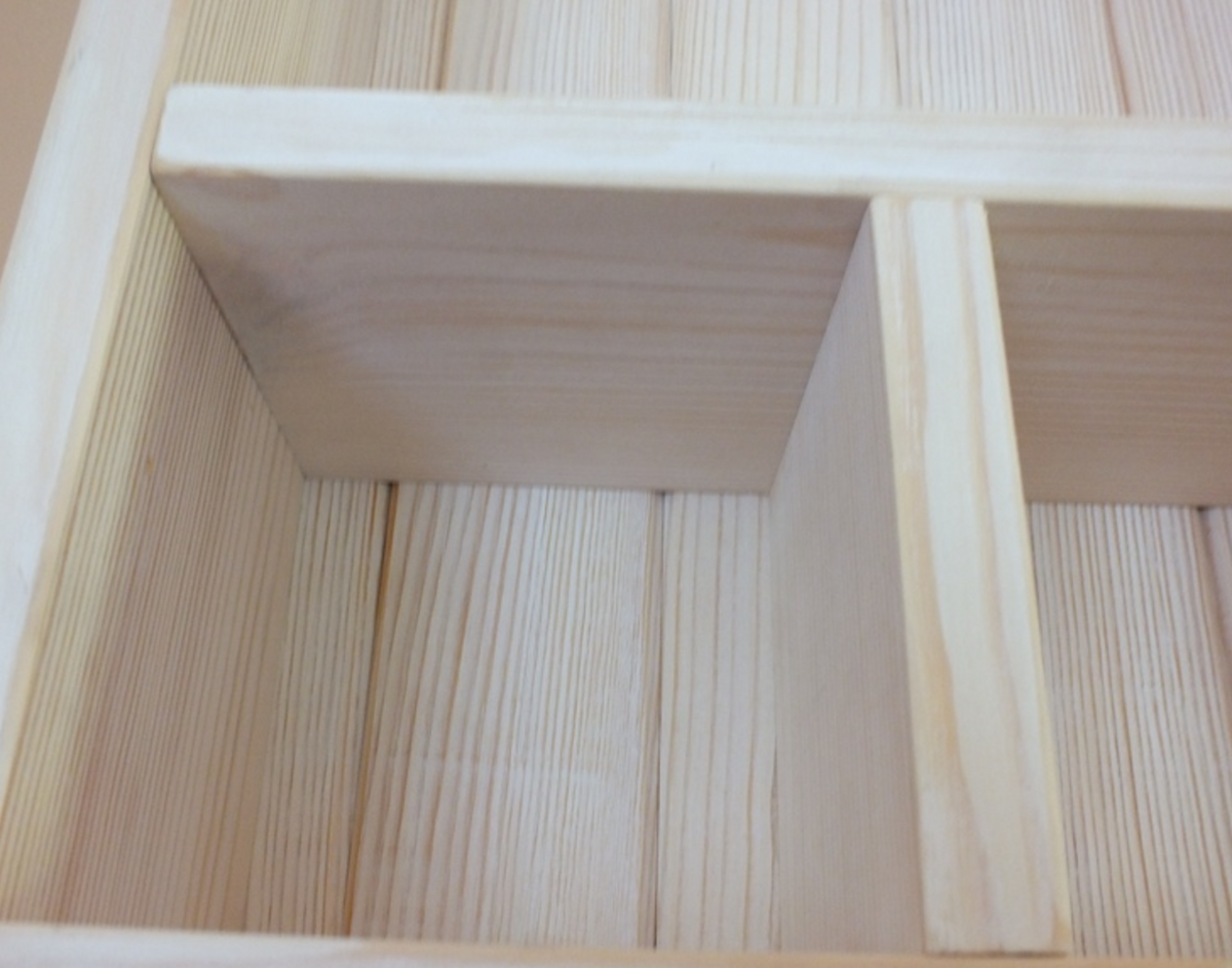 Close-up of a light natural wood shelf or cabinet divider with visible wood grain and three vertical compartments.