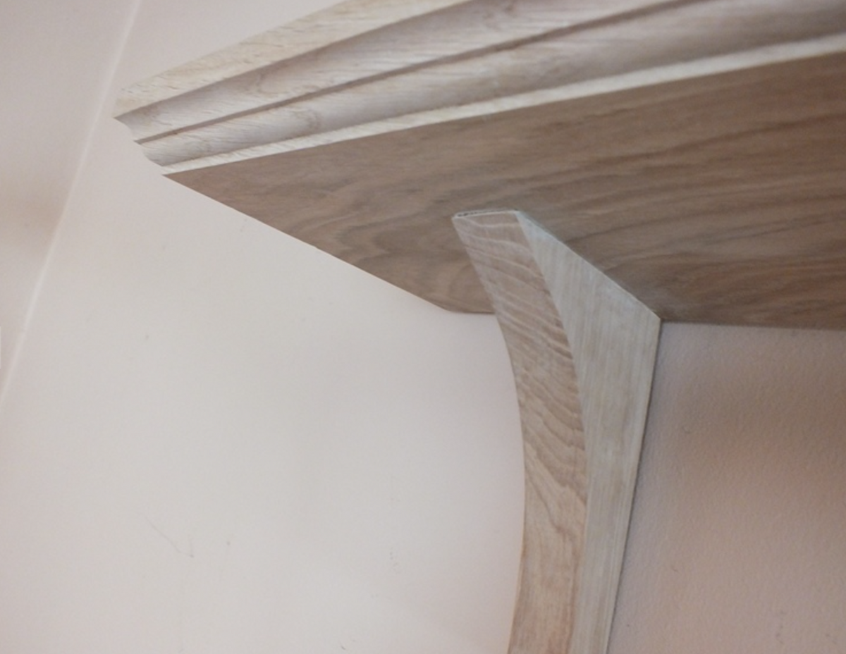 Close-up of a light natural wood shelf bracket mounted against a plain off-white wall.