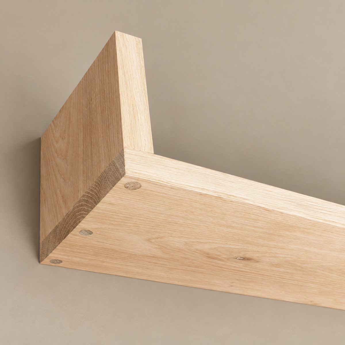 A close-up of a light natural wood shelf bracket corner with visible wood grain and pre-drilled screw holes, mounted against a plain warm beige wall.