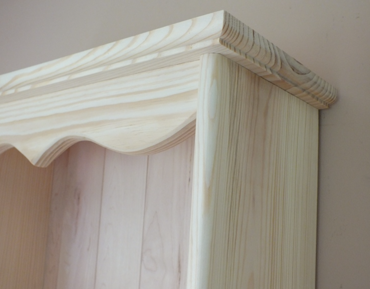 Close-up of a wooden shelf with a scalloped edge against a plain background