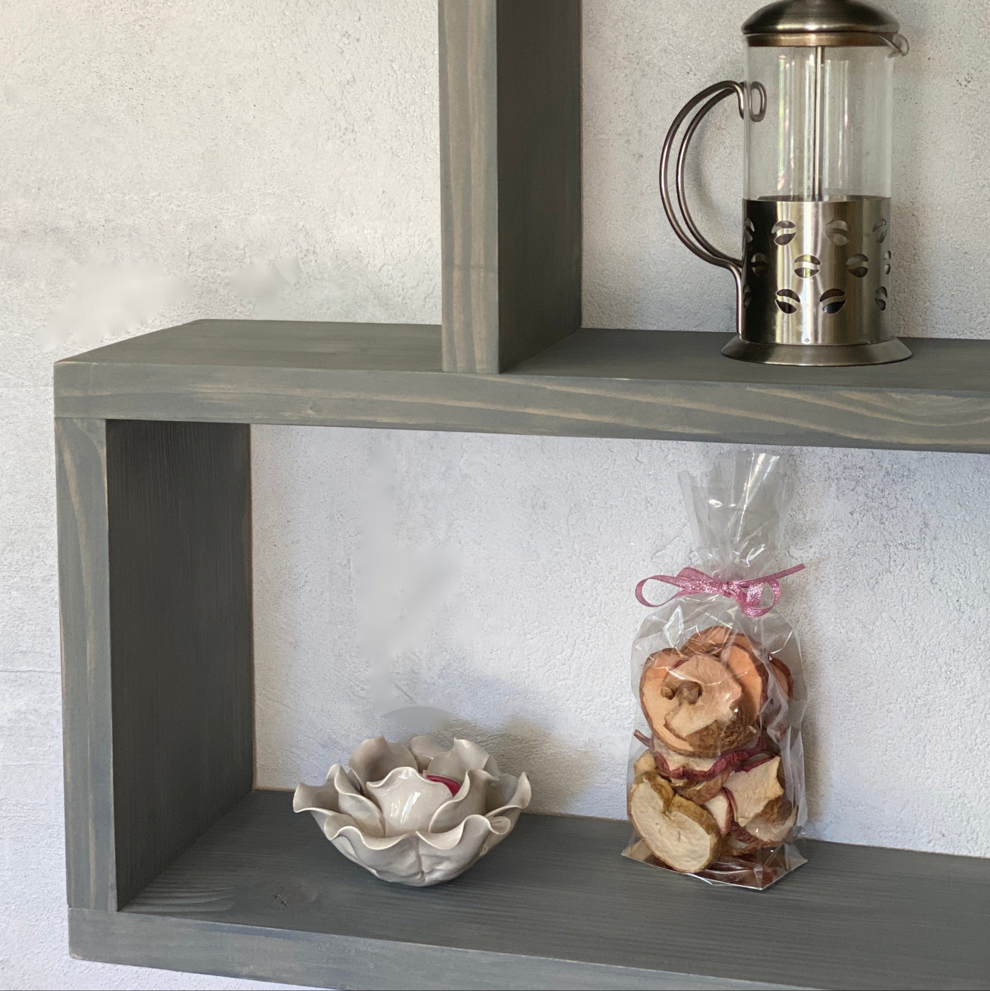 Gray corner shelf with a French press, cookies, and a decorative bowl against a light gray wall.