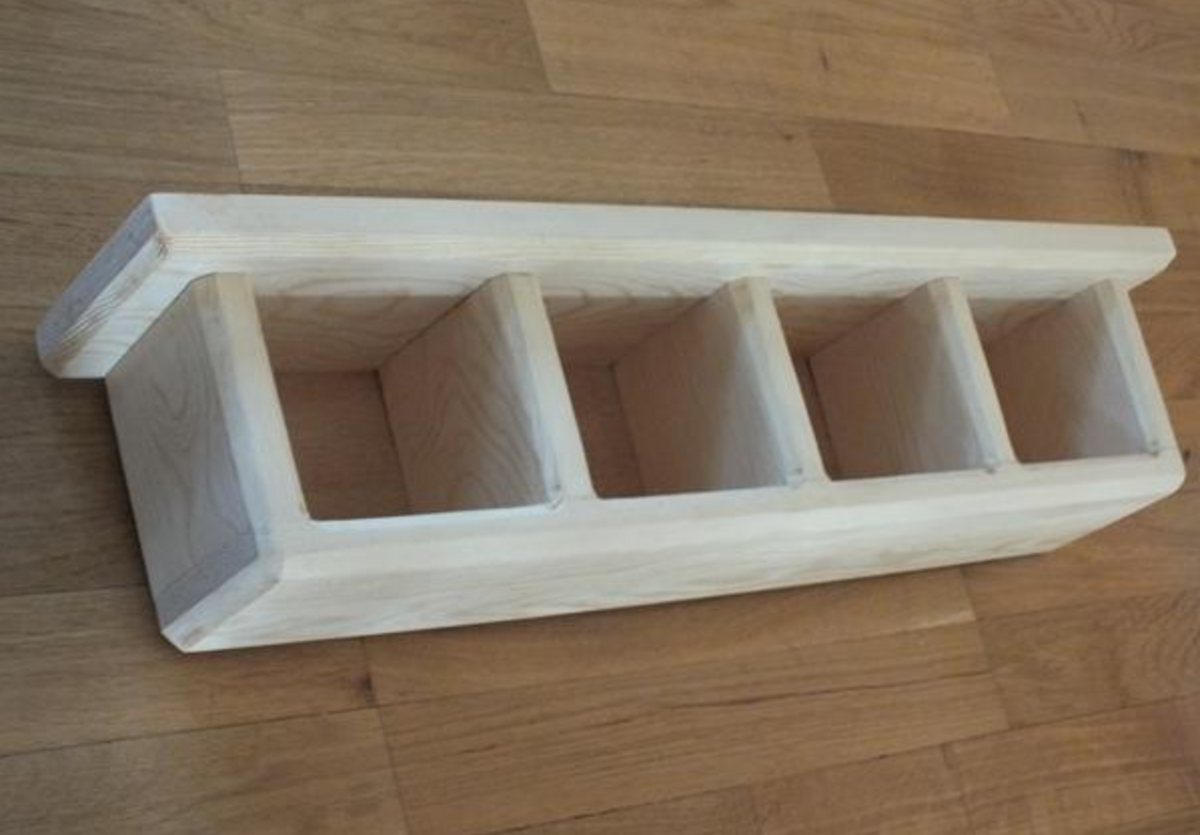 A light natural wood four-compartment organizer shelf with a slanted front, shown on a wooden floor.