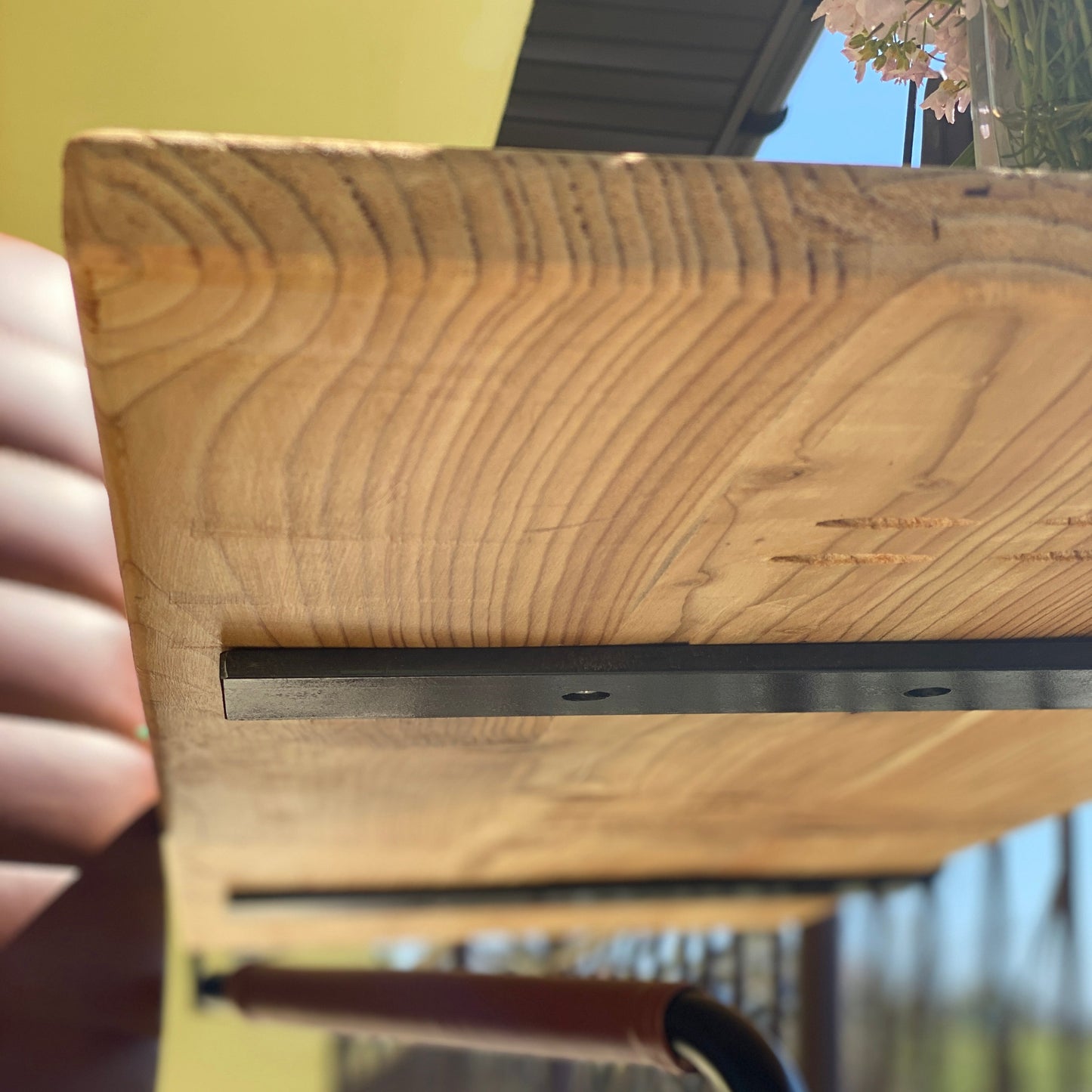 Wooden shelf with metal bracket held by a hand, blurred outdoor background