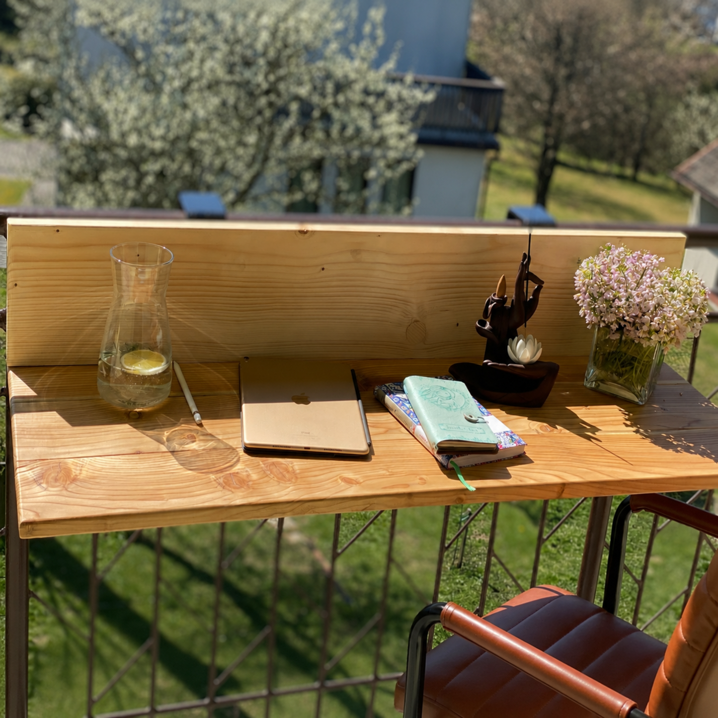 Wooden outdoor desk with a laptop, notebook, and decorative items on a grassy background