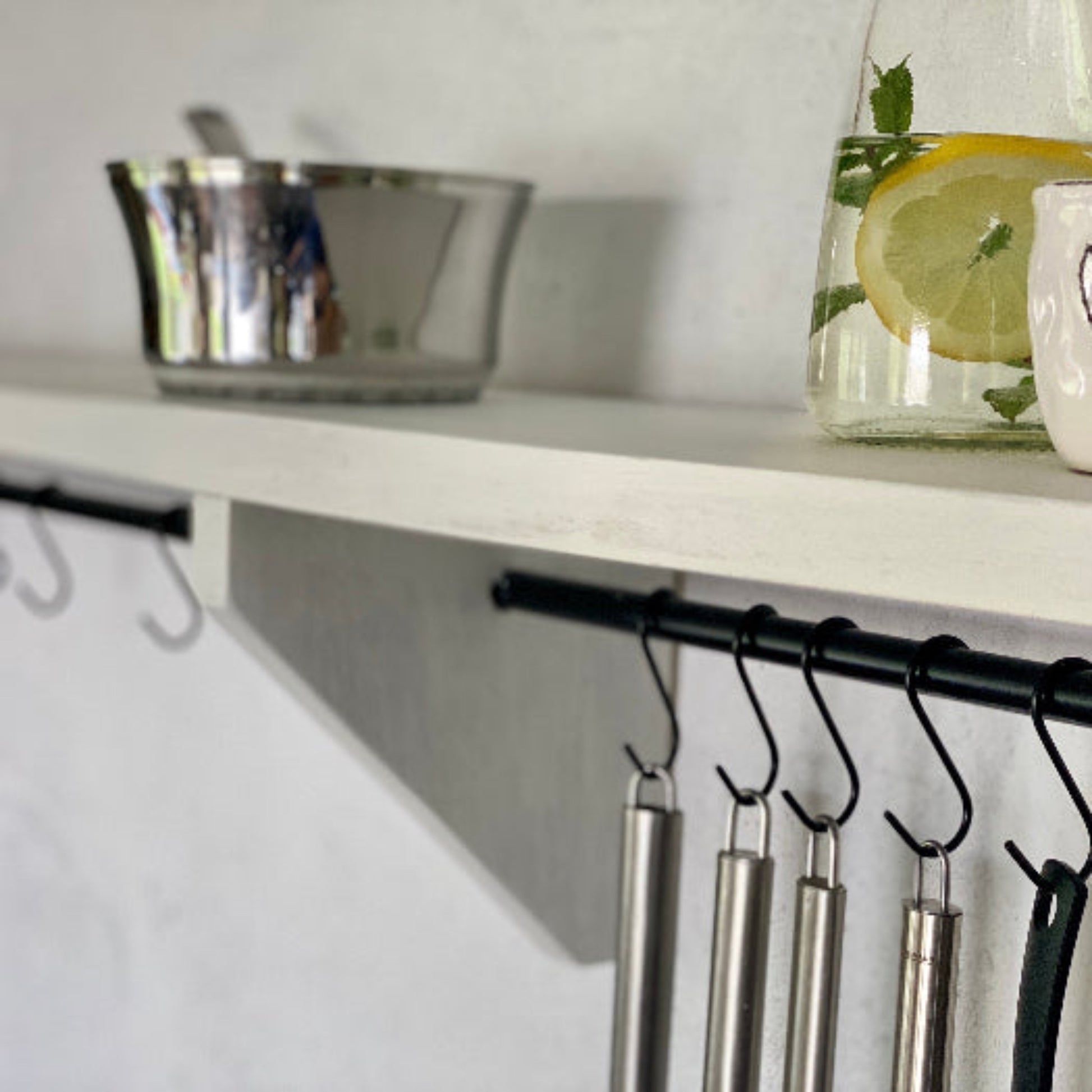 White shelf with kitchen items including a glass with lemon slices, a metal bowl, and a ceramic mug with a heart design.