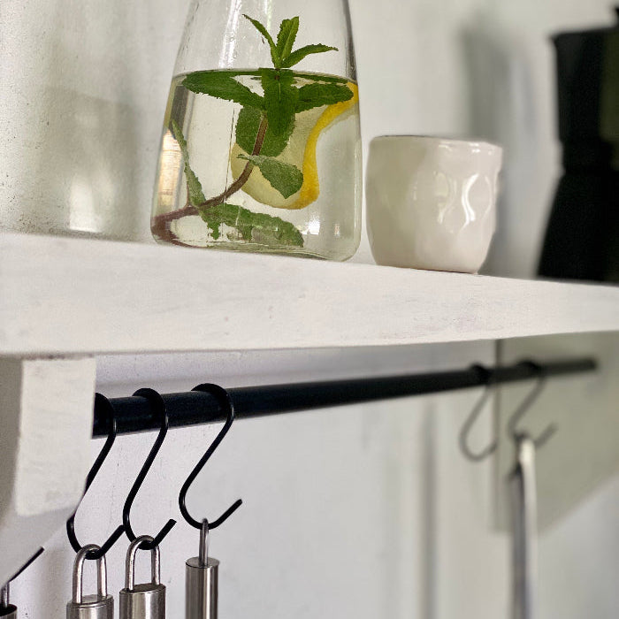 Clear vase with water, lemon, and mint leaves on a white shelf with kitchen utensils below.