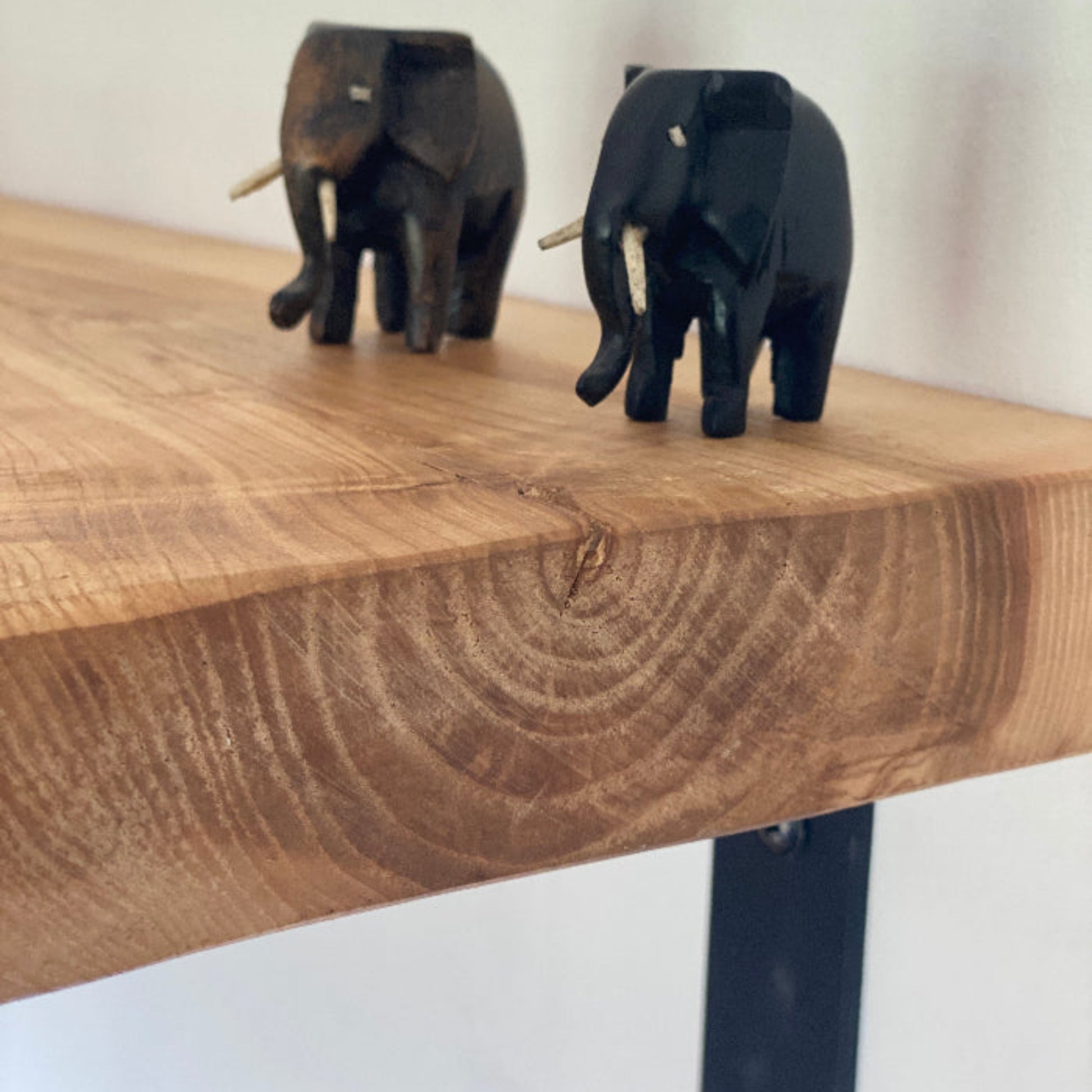Two small elephant figurines on a wooden surface with a white background